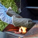 A person wearing Choice flame retardant oven mitts cooking meat on a grill.