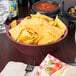 A raspberry polyethylene large round basket filled with tortilla chips on a table in a Mexican restaurant.