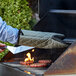 A person using a SafeMitt oven glove to cook burgers on a grill.