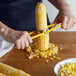 A person using a Fox Run corn stripper to cut a corn cob.