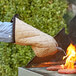 A person holding a Flame Retardant oven mitt over a grill.