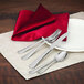 A table set with a red napkin and silverware including a Walco Cohasset cocktail fork.