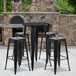A Flash Furniture black metal bar height table with black square seat backless stools in front of a stone fireplace.
