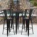 A Flash Furniture black metal bar height table with 4 black metal bar stools on an outdoor patio in front of a pool.