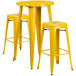 A yellow metal round bar height table with two square seat yellow metal backless stools.