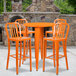 An orange metal Flash Furniture bar table and chairs on an outdoor patio.