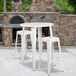 A white metal Flash Furniture bar table with 2 white square seat backless stools on an outdoor patio.