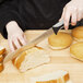 A person cutting a loaf of bread with a Dexter-Russell scalloped bread knife.