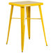 A yellow metal square bar height table with yellow metal stools.