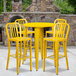 A yellow metal bar height table with 4 yellow chairs with vertical slat backs.
