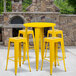 A group of yellow metal backless bar stools around a table.