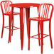 A red metal bar table with two red chairs with vertical slat backs.