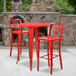 A Flash Furniture red metal bar height table with two red metal bar stools on an outdoor patio.