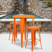 An orange Flash Furniture bar table with two square stools on an outdoor patio.