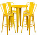 A yellow metal bar height table surrounded by four yellow metal bar stools.