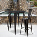 A Flash Furniture black metal bar table with two black metal bar stools on an outdoor patio.