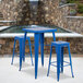 A blue metal table with two blue metal bar stools.