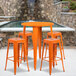 An orange metal bar height table with 4 square stools.