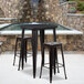 A Flash Furniture black metal bar height table with two square stools on an outdoor patio.