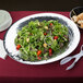 An American Metalcraft hammered stainless steel oval bowl filled with salad and a plate of bread.