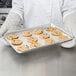 A person in gloves holding a Chicago Metallic aluminum sheet pan of cookies.