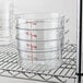 A stack of clear Cambro food storage containers with red writing on them on a metal rack.