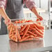 A woman holding a clear Cambro food storage box filled with carrots.