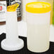 A white Carlisle plastic container with a yellow lid and spout.
