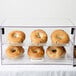 A Cal-Mil two-tier acrylic display case filled with bagels and donuts.