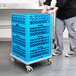 A man pushing a Cambro dish and glass rack dolly with a stack of blue crates.