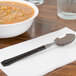A bowl of soup with a WNA Comet Reflections Duet stainless steel look plastic teaspoon on a napkin.