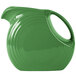 A white china pitcher with a green disc and handle.