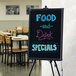 A black LED write-on board with food and drink specials written on it on a table.