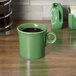 A green Fiesta china mug with a brown liquid on a wood surface.