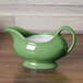 A green Fiesta gravy boat with a handle on a wood surface.