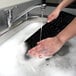 A person washing a Kensington ProFit Washable USB Keyboard in a sink.
