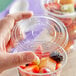 A hand holding a Choice clear plastic lid on a plastic container of fruit with red and orange fruit inside.