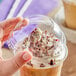 A hand holding a Choice clear plastic cup with whipped cream and chocolate on a drink.