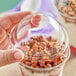 A hand holding a plastic container with granola in it and a clear plastic dome lid.