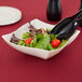 A Fineline ivory plastic serving bowl filled with salad, tomatoes, and lettuce with black tongs.