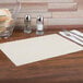 An ecru Hoffmaster paper placemat with a scalloped edge on a table with silverware.