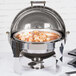 A Vollrath New York Roll Top Round Chafer with Brass Trim open on a silver pot.