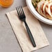 A black plastic Visions fork on a napkin next to a plate of food.