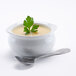 A bowl of Silver Skillet cream of chicken soup with a sprig of parsley on top with a silver spoon on the side.