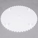 A white round Wilton cake separator plate with scalloped edges and three holes.