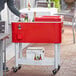 A man using a red Choice beverage cooler cart to hold bottles of drinks on a brick surface.