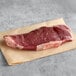 A piece of Warrington Farm Meats raw New York strip steak on a piece of paper.
