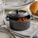 A Vollrath pre-seasoned cast iron pot of chili with a lid on a table with a fork, bread, and beans.