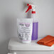 A white bottle of Noble Chemical restroom cleaner next to a purple and white packet kit on a white surface.