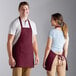 A man and a woman wearing Choice burgundy bib aprons standing at a kitchen counter.